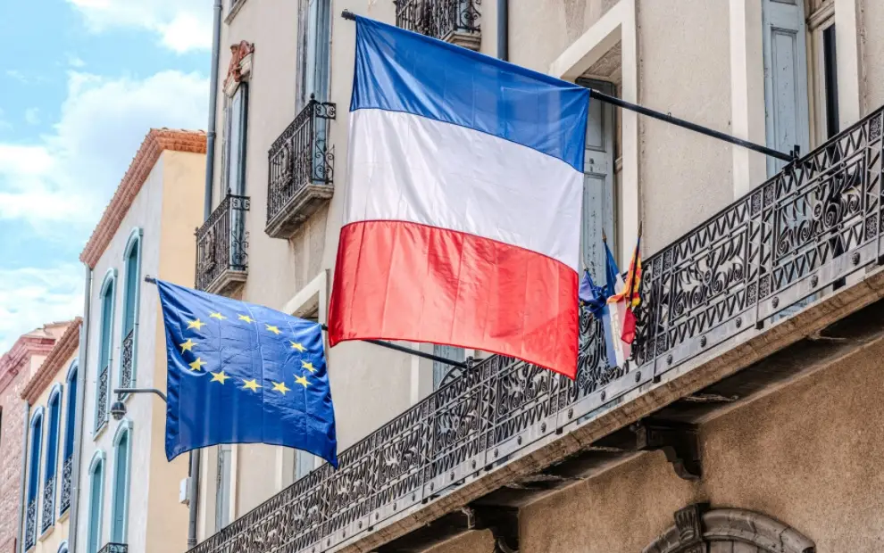 French and European Union flags hanging from the balconies of a building.